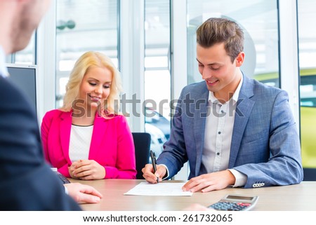 Couple buying car at dealership and signing sales contract with salesman