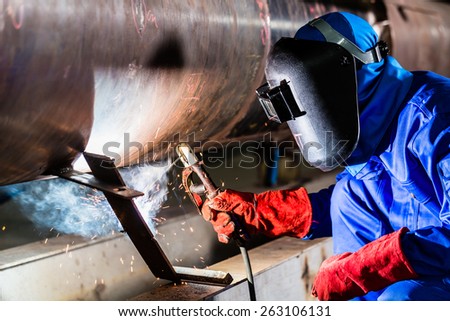 Welder in factory welding metal pipes