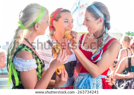 Friends visiting together Bavarian fair in national costume eating grilles sausage in bread roll