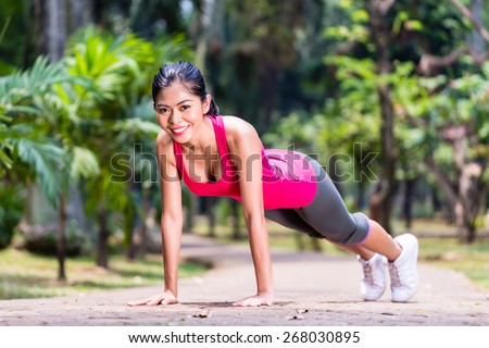 Proud and successful woman doing sport push-up in tropical Asian park, looking in camera during her exercise
