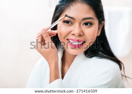 Asian woman in bathroom plucking eyebrows