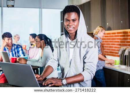 Black programmer in lounge of IT start-up coding software on his laptop, colleagues in the background