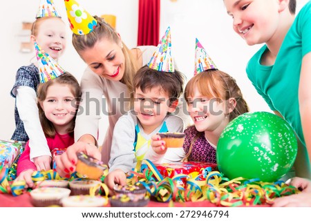 Children at birthday party grabbing muffins and cake, the kids are wearing hats, balloons and paper streamers for decoration