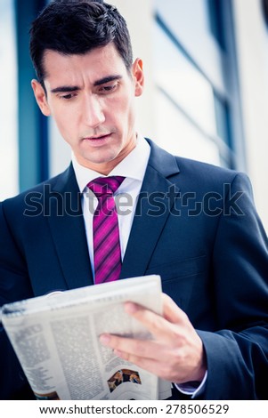 Man in suit reading newspaper outdoors in front of office building