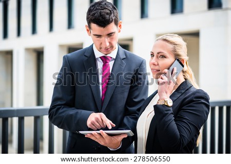 Business man and woman working outdoors with tablet computer in front of office building