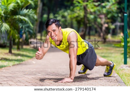 Proud and successful man doing sport push-up in tropical Asian park giving the thumbs-up sign