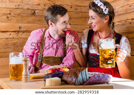 Couple having dinner at mountain hut in alps drinking beer and eating cold cuts
