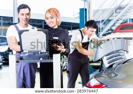 Asian Chinese car mechanic team checking auto engine with diagnostics tool in his workshop