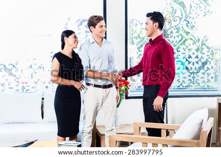 Mixed couple in furniture store with Asian shop assistant shaking hands sealing deal