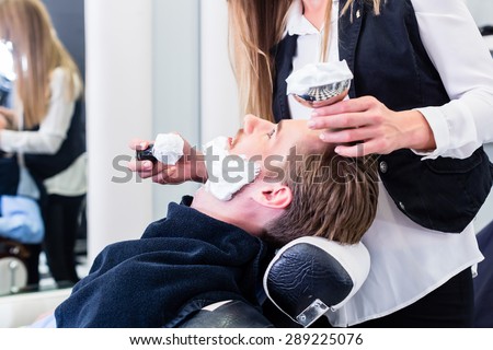 Woman barber shaving customer in her shop, applying soap with a brush
