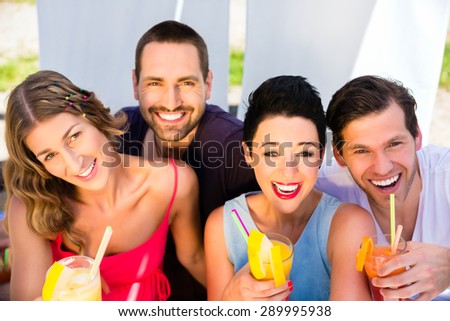 Group of friends, men and women, drinking cocktails in beach bar