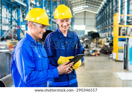 Two workers in production plant as team discussing, industrial scene in background