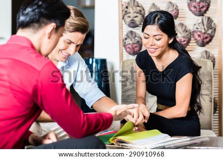 Couple of Caucasian man and Asian woman and shop assistant in furniture store planning furnishing of home together
