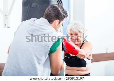 Senior woman with trainer in boxing sparring hitting sandbag