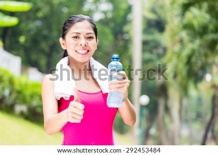 Asian woman having successful sport training giving thumbs up with water bottle in her hands