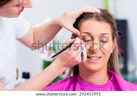 Woman with beautician in cosmetic salon receiving makeup