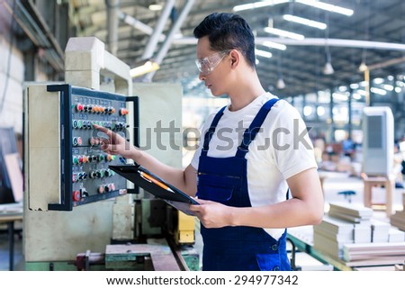 Worker pressing buttons on CNC machine control board in Asian factory