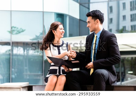 Asian business men and woman outside in front of tower building shaking hands