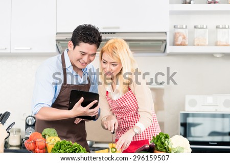 Asian couple cooking after recipes from tablet computer