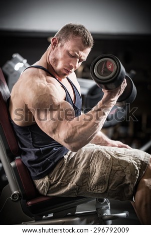 Man at fitness training with dumbbells in gym sitting on a weight bench