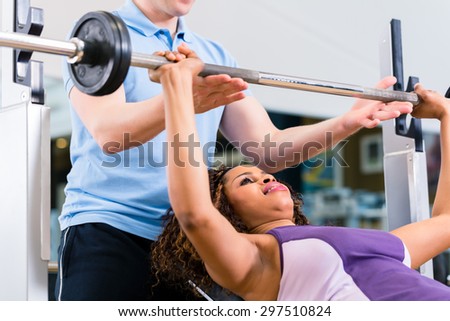 Black woman with Trainer lifting weights on barbell in gym for fitness