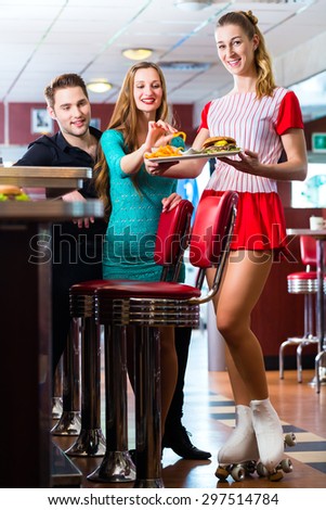 Friends or couple eating fast food in American fast food diner, the waitress wearing a short costume and roller skates
