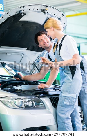 Male and female mechanic team examine car engine with light and checklist in workshop