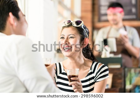 Asian couple, Indonesian woman and Korean man, in cafe flirting while drinking coffee, barista in the background