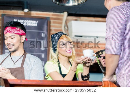 Asian Barista offering cafe to customer in coffee shop, another service worker preparing a drink