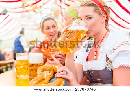 Women drinking Bavarian beer in tent on Oktoberfest or dult wearing dirndl