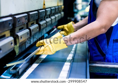 Asian worker in factory at metal skip machine putting work piece in