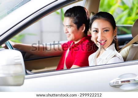 Asian couple driving new car on driveway to their home
