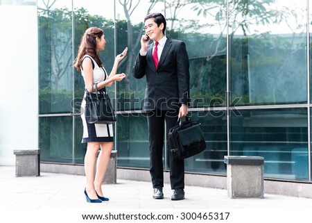 Asian business woman and man telephoning with mobile phone in front of building