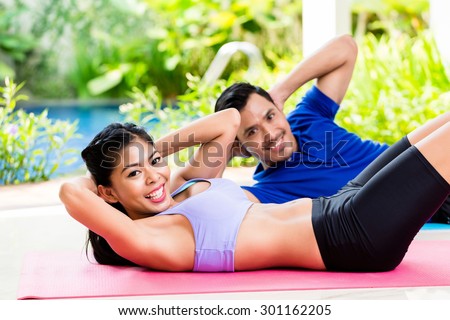 Asian fitness couple, man and woman, doing sit-up in tropical home