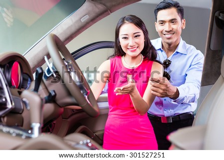 Asian couple choosing luxury car in auto dealership looking at the interior