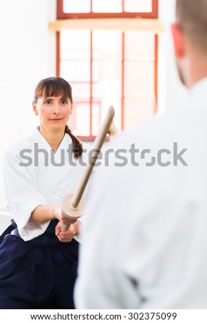 Man and woman fighting with wooden swords at Aikido training in martial arts school
