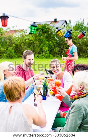 People toasting at party, in the background man at bbq grill with beer bottle in hand