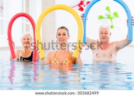 Group  or young and senior people in aquarobic fitness swimming pool exercising with  pool noodle