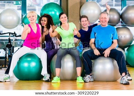 Men and women sitting on fitness balls in gym, diversity group of old, young, black and white people
