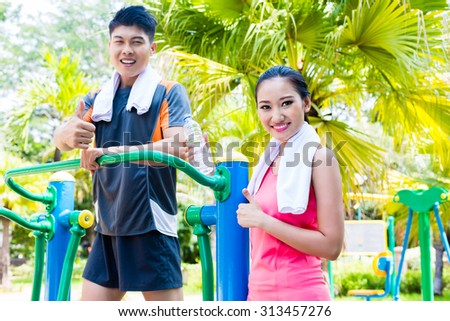 Asian Chinese man and woman training fitness on public cross trainer in outdoor gym