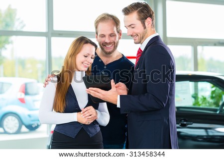 Seller or car salesman and clients or customers in car dealership presenting the interior decoration of new and used cars in the showroom on tablet computer