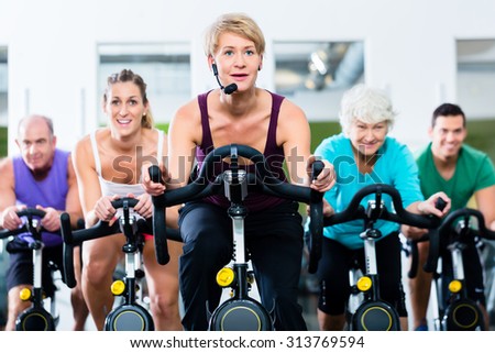 Senior and young people spinning on fitness bike in gym doing endurance and cardio training, the instructor is leading them on