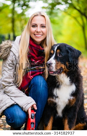 Woman cuddling with Bernese mountain dog in autumn park with colorful foliage, close up shot on head