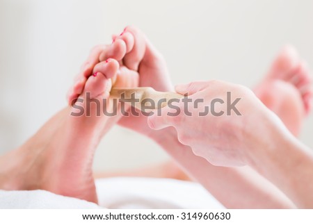 Women at reflexology having foot massaged or pressed with wooden stick