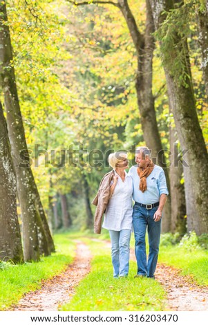 Senior woman and man, a couple, embracing each other having walk in the fall forest
