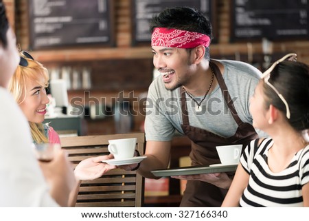 Waiter serving coffee in Asian cafe to women and man offering the drinks on a tray