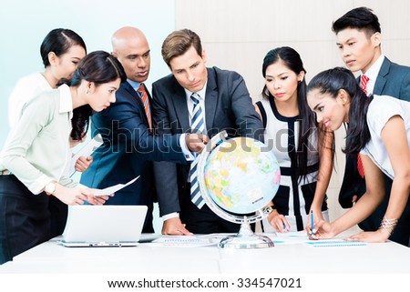Business team discussing available market intelligence for outsourcing plans looking at globe, Indian, Caucasian, Chinese and Indonesian people