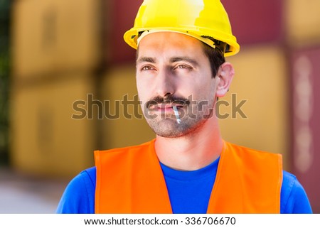 Smoking worker in logistics company with cigarette in front of containers