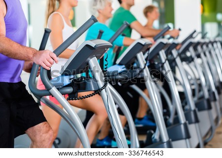 Group with senior and young men and women on elliptical treadmill trainer in fitness gym exercising