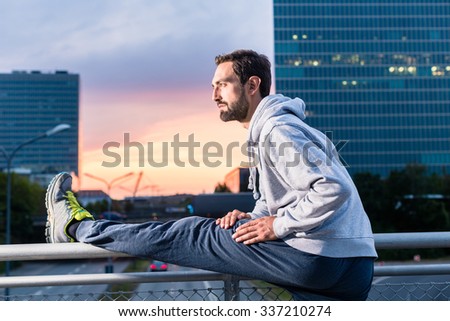 Runner stretching in front of office building at sunset